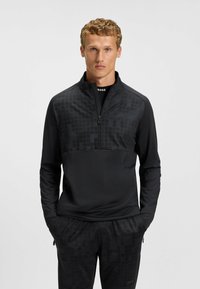 Pullover sportivo nero con zip a un quarto, caratterizzato da una parte superiore testurizzata con sottili motivi geometrici e maniche e corpo lisci.
