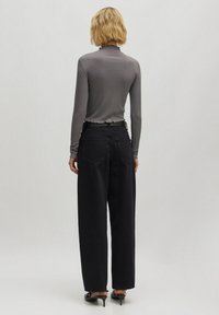 Graues Langarmoberteil mit wellenförmigem Ausschnitt, kombiniert mit weiten schwarzen Hosen und schwarzen High Heels. Der Blick von hinten zeigt die Taschendetails der Hose.