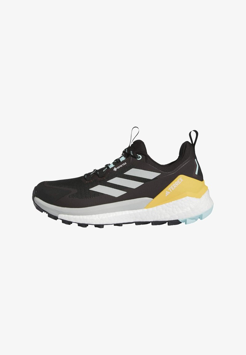 Czarne buty do biegania po szlakach z siateczkową cholewką, srebrnymi paskami, żółto-białą podeszwą środkową oraz teksturowaną gumową podeszwą dla lepszej przyczepności.