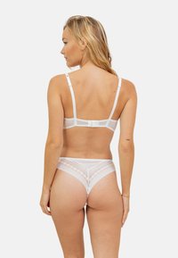 Ensemble de lingerie blanche comprenant un soutien-gorge transparent avec des bretelles réglables et une culotte assortie avec des détails en dentelle et des motifs géométriques.