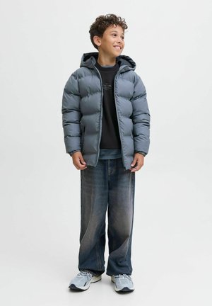 Grijze donsjack met een capuchon, rits aan de voorkant en elastische manchetten; gedragen over een zwart sweatshirt en gecombineerd met losse spijkerbroek en sneakers.