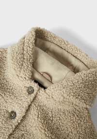 Giacca in pile beige con un esterno texture e soffice, grande colletto e due chiusure a bottone scure. Rivestimento interno morbido visibile.