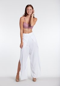 Roze gebloemd crop top met verstelbare bandjes, gecombineerd met hoge witte wijde broek met zijsplitten. Tan gekleurde sleehakken.