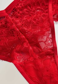 Rød blonde trusse med blomsterdesign, komplekse mesh detaljer og en glat talje. Teksturen er delikat og gennemsigtig.