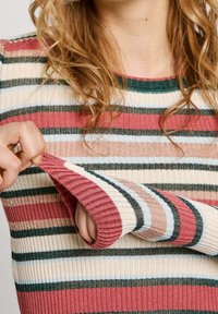 Pull à rayures avec une texture côtelée dans des tons crème, rose, sarcelle et marron. La manche est tirée pour dévoiler une main.