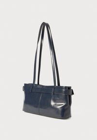 Navy blue leather tote bag with smooth texture, elongated shape, two long handles, and a central belt-like accent.