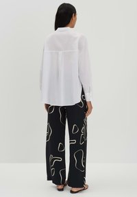 White long-sleeve shirt with a back yoke detail, paired with black wide-leg pants featuring beige abstract shapes. Smooth fabric texture.