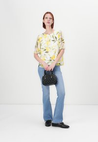 Blomsterbluse med gule sitron- og grønne bladmønstre, kombinert med lyseblå flagrende jeans og en liten svart teksturert håndveske.