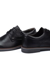 Chaussures en cuir noir avec une finition lisse, design à lacets, col rembourré et semelle contrastante marron. Présente des coutures discrètes et un détail de logo.