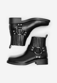Bottines noires à bout rond, en cuir texturé, avec deux accents de courroie et un petit talon carré. Présentent des accessoires en métal argenté et des rainures verticales.