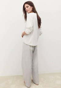 Top bianco a maniche lunghe abbinato a pantaloni larghi grigi con texture e un motivo sottile, visto da dietro.