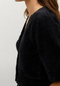 Cardigan nero peloso con maniche ampie, realizzato in materiale morbido. Senza chiusure; presenta una vestibilità rilassata e una superficie testurizzata.
