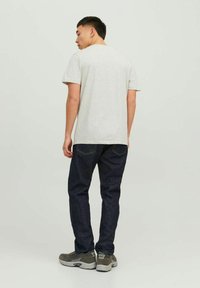 Grå bomulds t-shirt, kortærmet, parret med mørkeblå denim jeans. Model iført grå sneakers, set fra ryggen mod en ensfarvet baggrund.