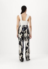 White smocked bodice with wide straps, paired with black and white patterned wide-leg pants featuring blue accents and a soft texture.