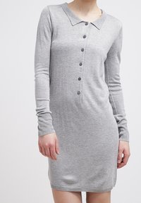 Abito grigio lavorato a maglia con colletto, maniche lunghe, bottoni frontali, polsini e orlo a costine. Texture morbida e forma aderente.