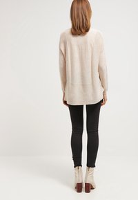 Jasnobeżowy, dziany sweter o luźnym kroju, długich rękawach i prostym tylnym brzegu, zestawiony z czarnymi, dopasowanymi spodniami oraz kremowymi botkami za kostkę.