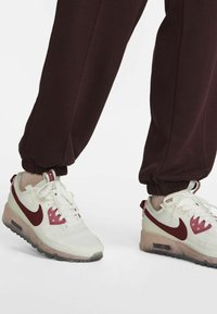 Nike Air Max sneakers with white and maroon colorway, featuring mesh and synthetic materials, visible air cushioning, and textured accents.