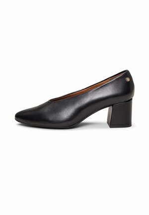 Zapato de mujer en piel negra con tacón bajo, punta redondeada y tacón ancho, con un pequeño emblema metálico decorativo cerca del tacón.