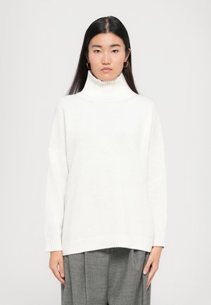 Pull en maille blanche avec col roulé, à la coupe décontractée, avec des poignets et un ourlet côtelés. Modèle portant un pantalon à carreaux gris. Tissu simple et texturé.