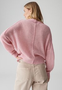 Maglione rosa lavorato a maglia con vestibilità ampia, spalle scese e finitura testurizzata. Abbinato a pantaloni beige chiaro, con tasche posteriori.