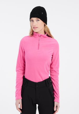 Suéter de forro polar en rosa brillante con cuello con cremallera, combinado con pantalones negros que presentan detalles de botones y cremallera. Material texturizado.