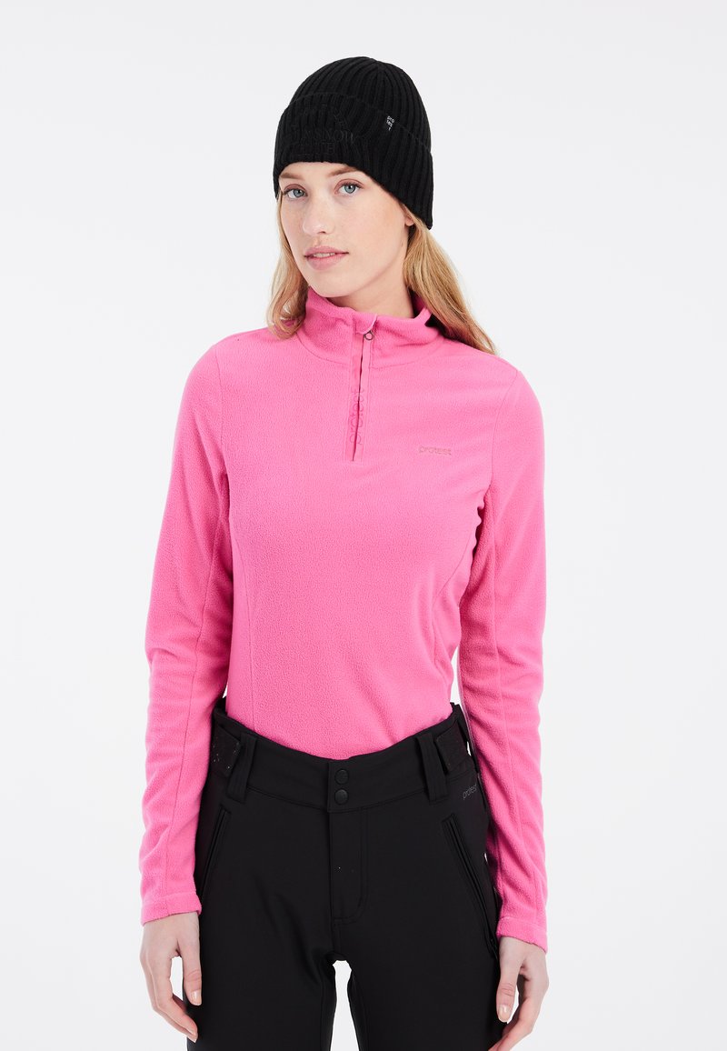 Pullover in pile di colore rosa brillante con colletto con zip, abbinato a pantaloni neri con dettagli in bottone e cerniera. Materiale tessurizzato.