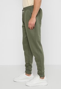 Pantalones jogger de color verde oliva, fabricados en una suave mezcla de algodón, con cinturilla elástica y cordón, bolsillos laterales y diseño de pierna cónica.