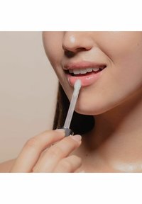 Aplikator przezroczystego błyszczyku do ust trzymany blisko warg, z przezroczystą rurką i białym końcówką aplikatora. Gładkie usta z błyszczącym wykończeniem.