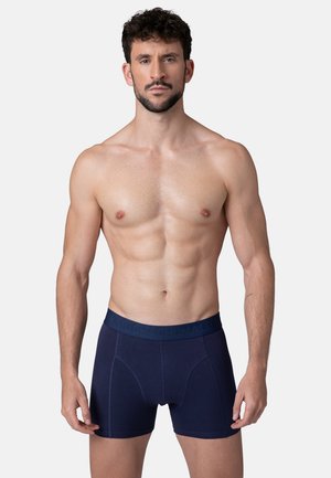 Sötétkék boxeralsó, szoros szabással. Puha anyagból készült, vastag derékrésszel, amelyen felszíni mintázat található. Az egész anyag sima tapintású.