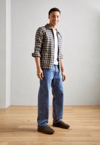 Camisa a cuadros en verde y púrpura, camiseta blanca, jeans azules y zapatos marrones. Textura suave, corte relajado y mangas arremangadas.