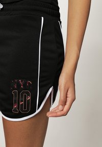 Černé sportovní šortky s bílým lemováním, na přední straně s reflexním vzorem "NYC" a "10". Viditelný elastický pas.