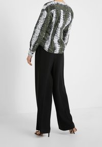 Haut multicolore avec des rayures verticales vertes et blanches ; pantalon noir taille haute ; tissu lisse, coupe ample, manches à longueur de poignet, talons hauts.