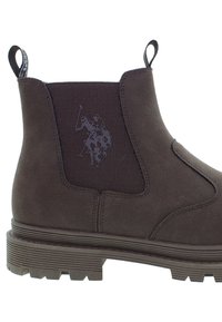 Stivale Chelsea in suede marrone con pannello elastico laterale che presenta il logo del giocatore di polo, linguette sul tallone e sul davanti, e suola in gomma spessa con scolpitura.