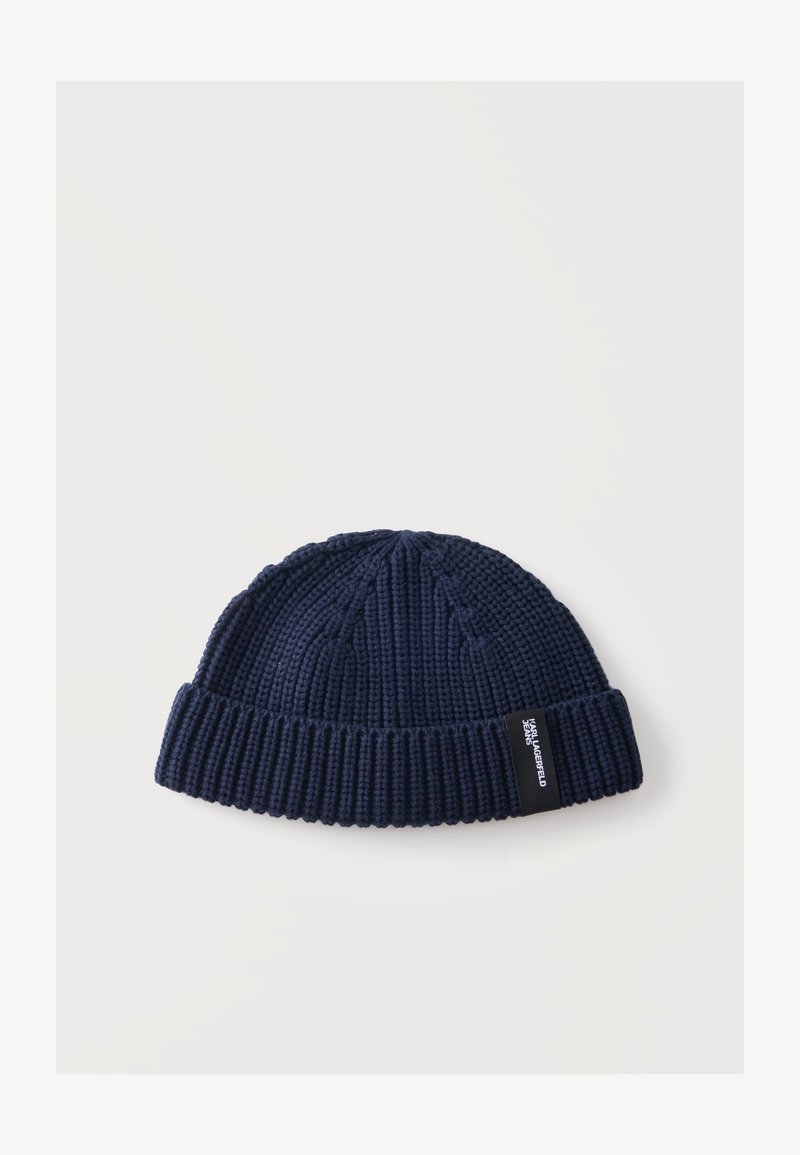 Bonnet tricoté bleu marine avec revers plié et étiquette noire sur le revers avec texte blanc.