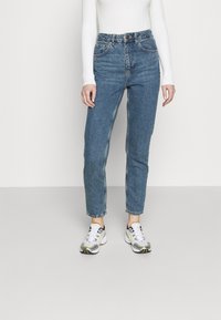 Höga blå denimjeans med rak ben, som har fem fickor och dragkedja. Kombination med svarta och vita sportskor.