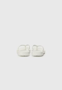 Weiße Sandalen mit minimalistischem Design, weichem Material und flexibler Sohle mit einem Profilmuster für besseren Halt. Zwei schmale Riemen an der Oberseite.