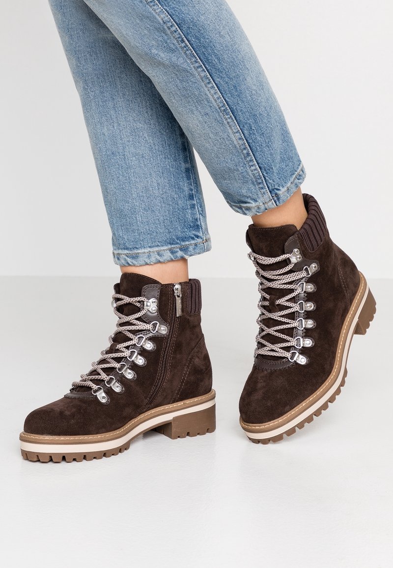 Brązowe zamszowe botki za kostkę z żebrowanym kołnierzem, metalowymi oczkami i kontrastującą podeszwą. Posiadają zamek błyskawiczny z boku dla łatwego zakładania.