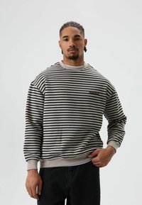 Gestreepte sweater in beige en zwart, met ronde hals, geribbelde manchetten en zoom. Voorzien van een klein rood logo op de borst. De stof is zacht.