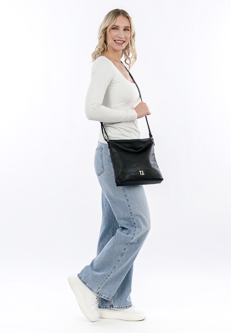 Schwarze Leder-Crossbody-Tasche mit einem goldenen Monogramm "TL", das eine weiche Textur, rechteckige Form und verstellbaren Schulterriemen aufweist.