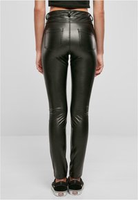 Zwarte faux leren high-waisted broek heeft een strak silhouet met achterzakken en een glanzende textuur. Draag het met zwarte sneakers.