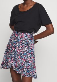 Svart kortärmad t-shirt i kombination med en blommig omslagskjol med marinblå bakgrund, rosa och blå blommor samt en volangkant.