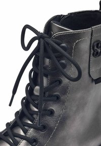 Botín de cuero negro hasta el tobillo con punta redonda, cordones planos negros, ojales de metal y un acabado elegante. Cuenta con un collar acolchado para mayor comodidad.