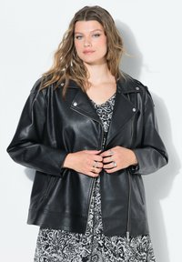 Chaqueta de cuero negra de motociclista con un corte oversize, cierre con cremallera, grandes solapas y herrajes plateados. Llevada sobre un vestido estampado.