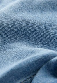 Tecido de denim de uniesc blu cu o textură vizibilă de țesătură în diagonală. Aspect neted și ușor șifonat, cu detalii subtile de coasere.
