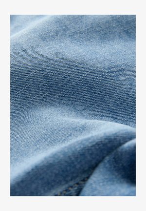 Tela de mezclilla azul claro con una textura de sarga visible. Apariencia suave y ligeramente arrugada con un detalle de costura sutil.