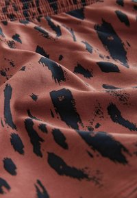 Katoenen stof in een warme terracotta kleur met abstracte zwarte penseelstreken; gestructureerd oppervlak met detail van een gerimpelde tailleband.