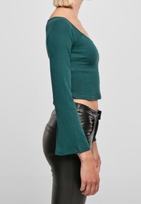 Tyrkysový žebrovaný top s dlouhým rukávem, V-výstřihem a rozšířenými rukávy, doplněný černými slim fit koženými kalhotami. Jednoduchý design a hladká textura.