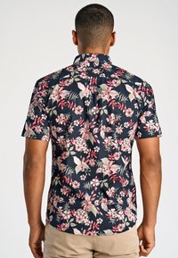 Koszula z krótkim rękawem o granatowym tle z kwiatowym wzorem w odcieniach różu i zieleni. Lekki materiał, luźny krój i kołnierz zapinany na guzik.