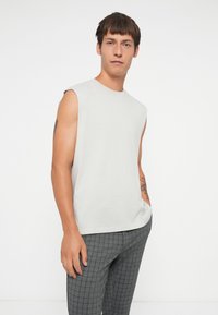 Camisa sin mangas de color gris claro en un material suave, combinada con pantalones de cuadros grises; textura suave y corte relajado, diseño minimalista.