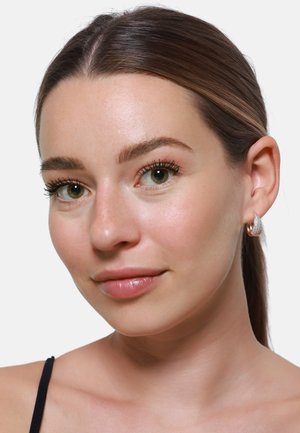 Ohrringe aus Roségold in Form von Creolen mit strukturierten Oberflächen und glänzendem Finish, getragen von einem Model mit glattem Haar vor einem neutralen Hintergrund.